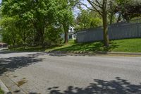 a sidewalk with green grass and a fence in front of a house with a large tree