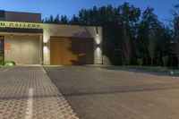 a lighted garage with plants on the side and a driveway leading into the entrance of an art gallery at night