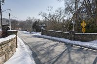 an empty street is lined with snow on the ground next to some buildings and a small stone fence