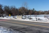 a traffic signal sits in the snow near the road side at a stop sign near a lake