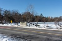 a traffic signal sits in the snow near the road side at a stop sign near a lake