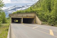 a large open entrance to a large tunnel next to mountains with snow on top and on both sides of the road