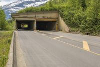 a large open entrance to a large tunnel next to mountains with snow on top and on both sides of the road