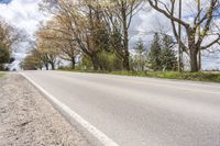 an empty country road near a grove of trees and grass against a blue sky with white clouds