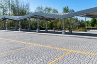 empty parking lot with covered seating with open area for the buses or passengers, next to trees and benches