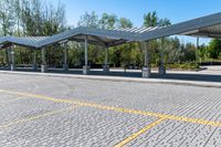 empty parking lot with covered seating with open area for the buses or passengers, next to trees and benches