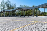 empty parking lot with covered seating with open area for the buses or passengers, next to trees and benches