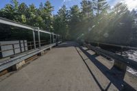 a paved bridge with benches on each side of the road near trees with bright sunlight