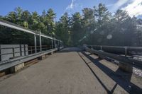 a paved bridge with benches on each side of the road near trees with bright sunlight