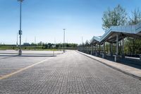 a view of a public transit station across a cobbled stone walkway in front of a large green field