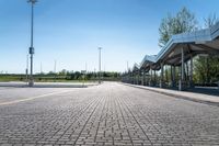 a view of a public transit station across a cobbled stone walkway in front of a large green field