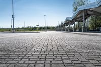 a view of a public transit station across a cobbled stone walkway in front of a large green field