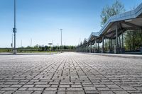 a view of a public transit station across a cobbled stone walkway in front of a large green field