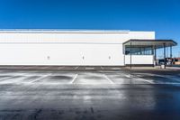 an empty parking lot with a white building in the background and a blue sky above the place