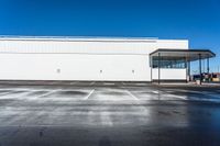 an empty parking lot with a white building in the background and a blue sky above the place