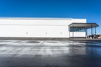 an empty parking lot with a white building in the background and a blue sky above the place