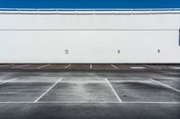 an empty parking lot with no cars in it in front of a building with white walls