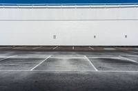 an empty parking lot with no cars in it in front of a building with white walls