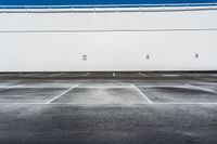 an empty parking lot with no cars in it in front of a building with white walls