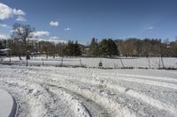 a field is covered in snow next to a park with trees, bushes and a fence