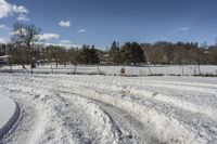 a field is covered in snow next to a park with trees, bushes and a fence