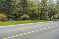 trees are standing on either side of a road, surrounded by fenced area with wooden fences