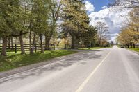 a lone road with a fence on both sides, leading to a pasture where the horse is standing in the middle