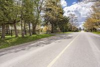 a lone road with a fence on both sides, leading to a pasture where the horse is standing in the middle