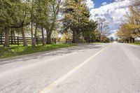 a lone road with a fence on both sides, leading to a pasture where the horse is standing in the middle