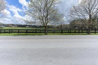 a horse standing next to a fence on a street in a pasture area with a road nearby