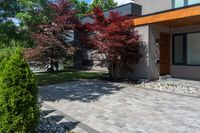 the front view of this modern home shows brick walkway, stone pavers, and colorful trees