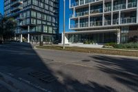 a street with an empty sidewalk and tall buildings in the background and one building has glass panels in the front and one has a glass bale windows