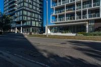 a street with an empty sidewalk and tall buildings in the background and one building has glass panels in the front and one has a glass bale windows