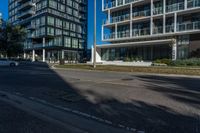 a street with an empty sidewalk and tall buildings in the background and one building has glass panels in the front and one has a glass bale windows