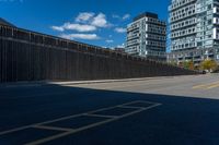 a paved street next to tall buildings and blue skies in the distance, and a bench in the middle