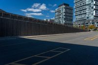 a paved street next to tall buildings and blue skies in the distance, and a bench in the middle