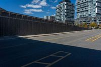 a paved street next to tall buildings and blue skies in the distance, and a bench in the middle