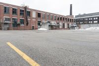 the empty parking lot has only snow on the ground in front of an old brick factory