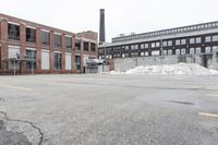 the empty parking lot has only snow on the ground in front of an old brick factory