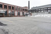 the empty parking lot has only snow on the ground in front of an old brick factory