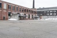 the empty parking lot has only snow on the ground in front of an old brick factory