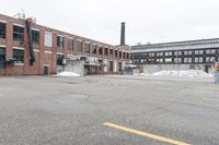 the empty parking lot has only snow on the ground in front of an old brick factory