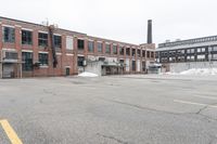 the empty parking lot has only snow on the ground in front of an old brick factory