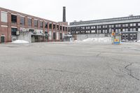 the empty parking lot has only snow on the ground in front of an old brick factory