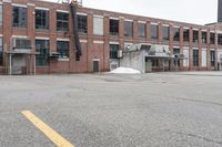 the empty parking lot has only snow on the ground in front of an old brick factory