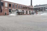 the empty parking lot has only snow on the ground in front of an old brick factory