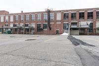 the empty parking lot has only snow on the ground in front of an old brick factory