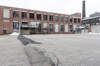 the empty parking lot has only snow on the ground in front of an old brick factory