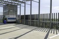 a blue and white bus is parked in front of a metal fence and a tall building