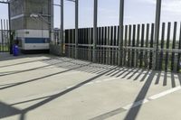 a blue and white bus is parked in front of a metal fence and a tall building